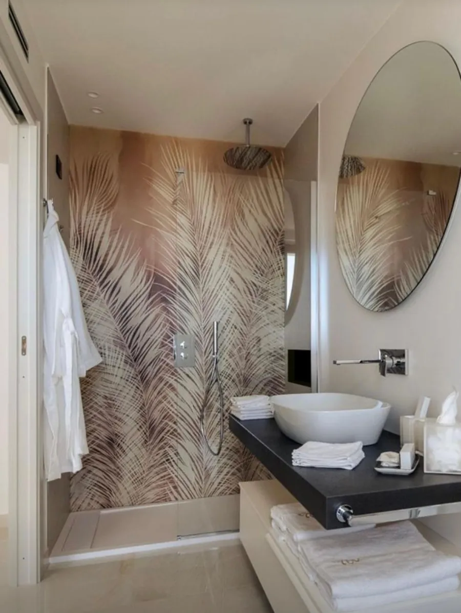 Bagno con la parete della doccia rivestita di foglie di palma su fondo ramato