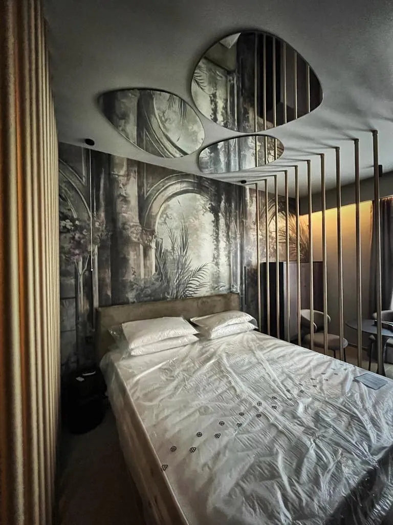 Camera con carta da parati ad archi e vegetazione dietro il letto